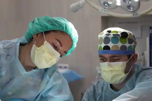 Ein Arzt und eine Ärztin in OP-Kleidung und mit Schutzmasken nehmen eine njicht näher erkennbare Operation vor